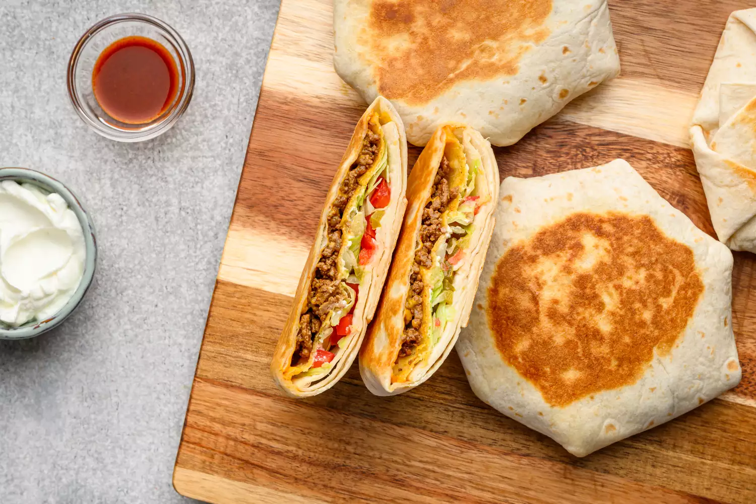 Une planche à découper avec des Crunchwrap Supremes dorés, coupés en deux, servis avec de la sauce piquante