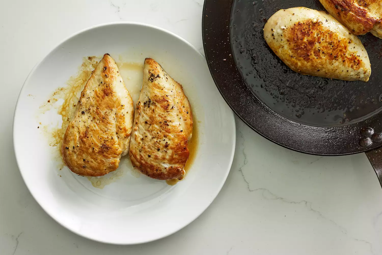 A skillet with two cooked chicken breasts, and a plate with two cooked chicken breasts