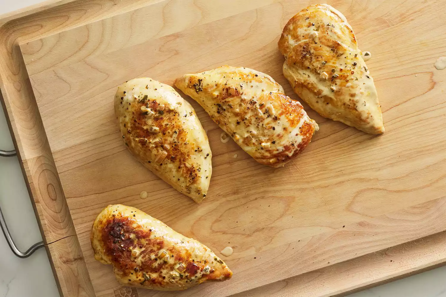Four cooked chicken breasts on a wooden cutting board