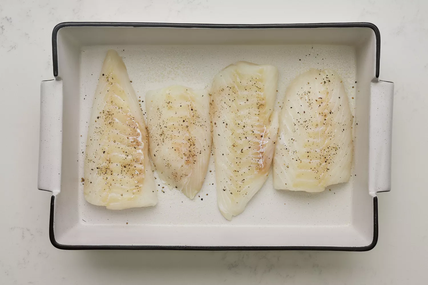 Un plat avec quatre filets de morue, saupoudrés de sel et de poivre noir