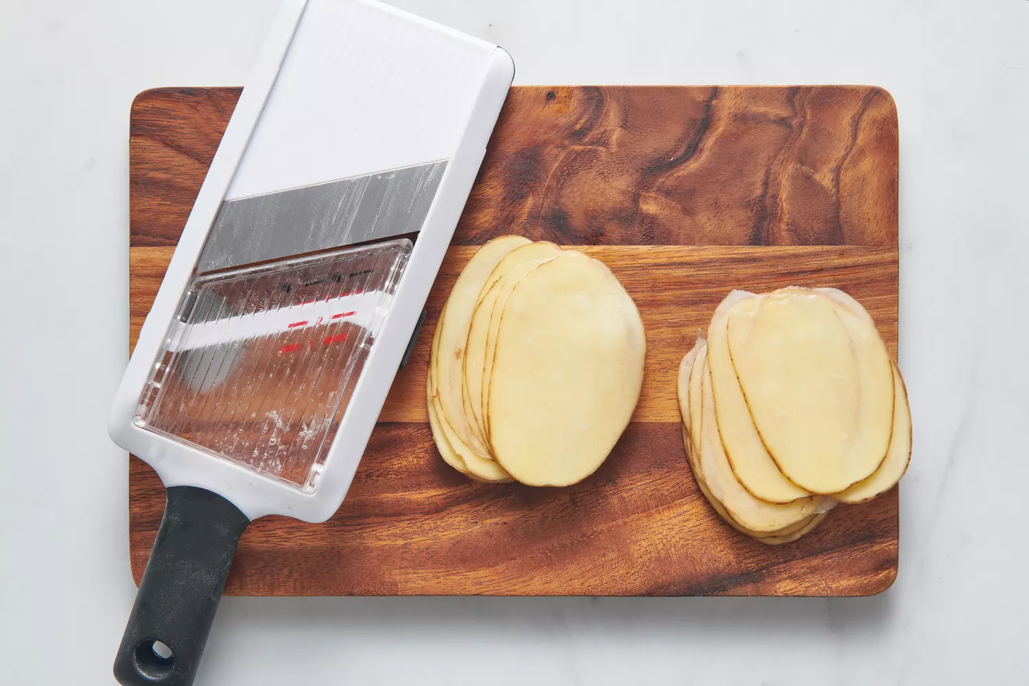 Une planche à découper et une mandoline avec des pommes de terre très finement tranchées