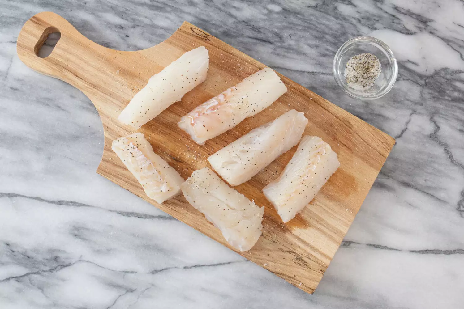 cut fish pieces on a cutting board with salt and pepper