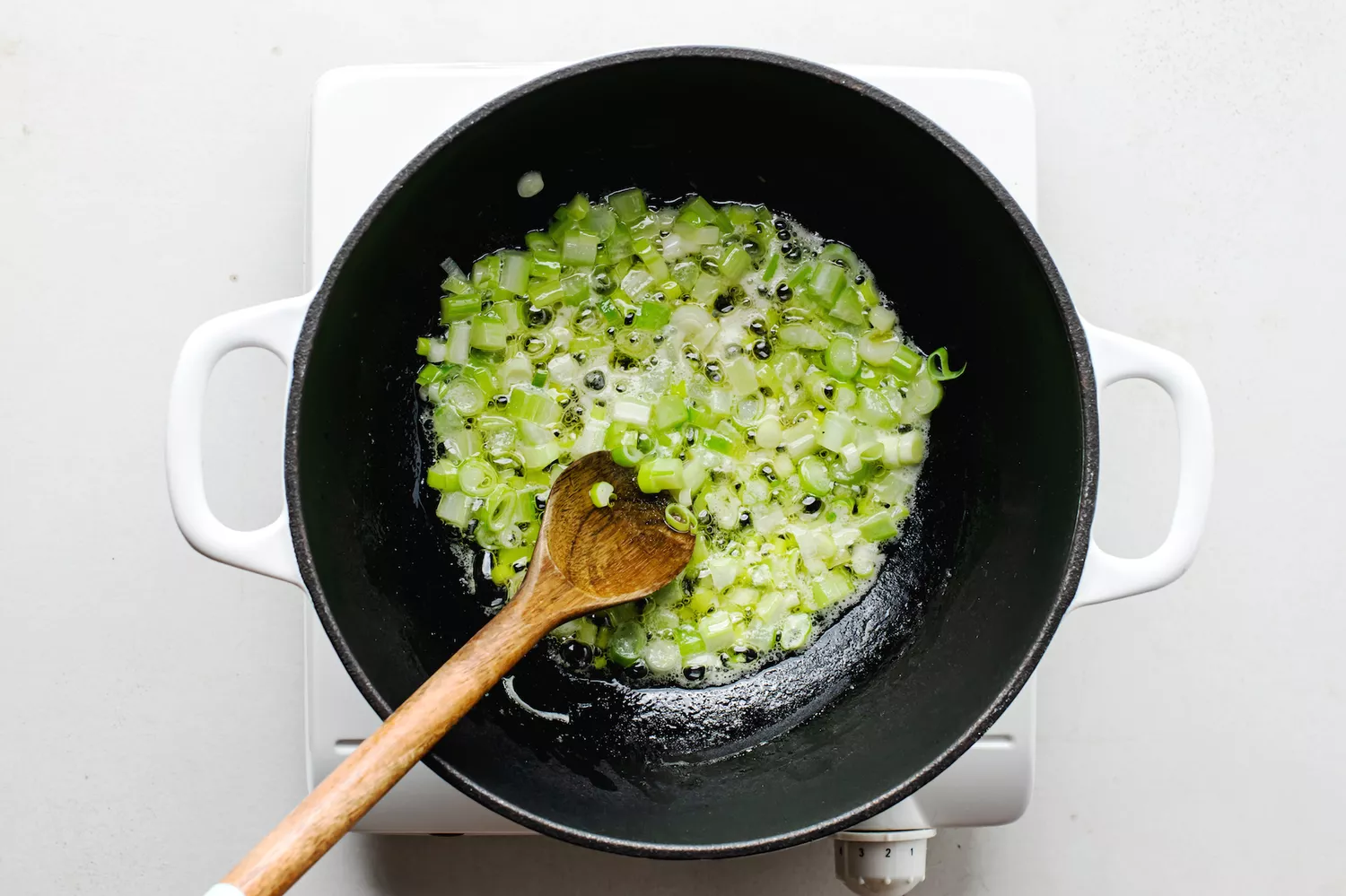 Oignon vert et céleri dans du beurre fondu dans une casserole
