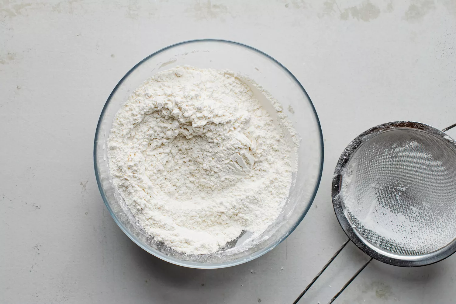 Farine, levure chimique et sel tamisés dans un bol en verre avec un tamis en maille