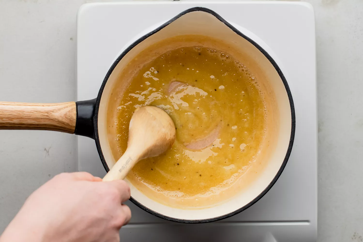 Molho em uma pequena panela sendo mexido com uma colher de pau no fogão