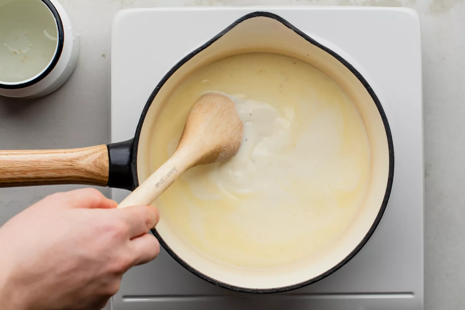 Leite sendo gradualmente misturado ao molho com uma colher de pau