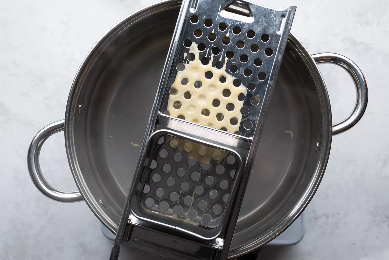 Pâte versée sur un mouleur de spaetzle sur une casserole avec de l'eau