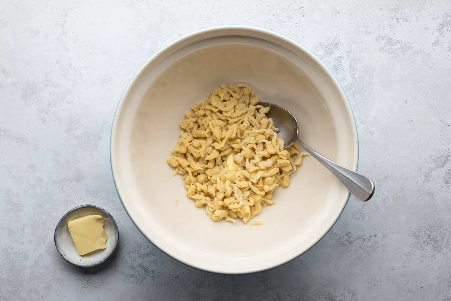 Spaetzle dans un bol avec une cuillère et du beurre dans un petit bol