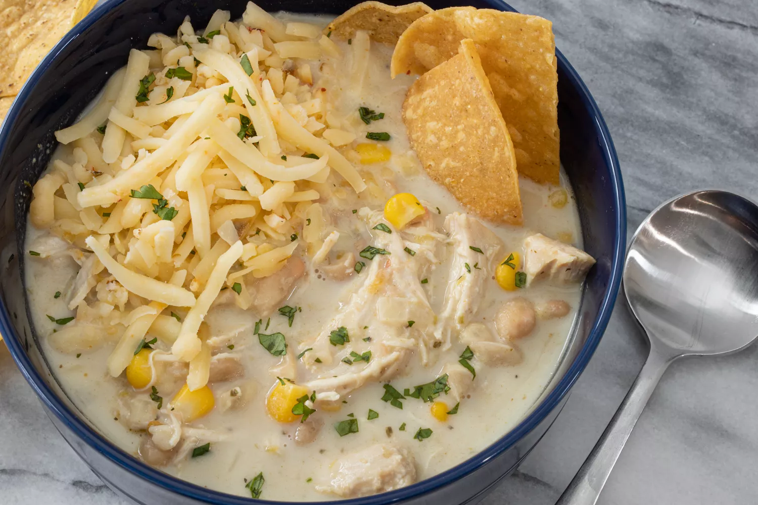 bowl of white chicken chili with extra cheese, cilantro, and tortilla chips