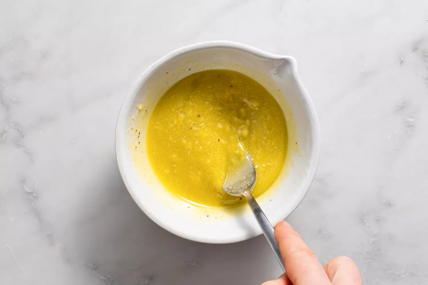 Ail, huile d'olive, jus de citron, moutarde de Dijon, sel, et poivre dans un bol avec une cuillère