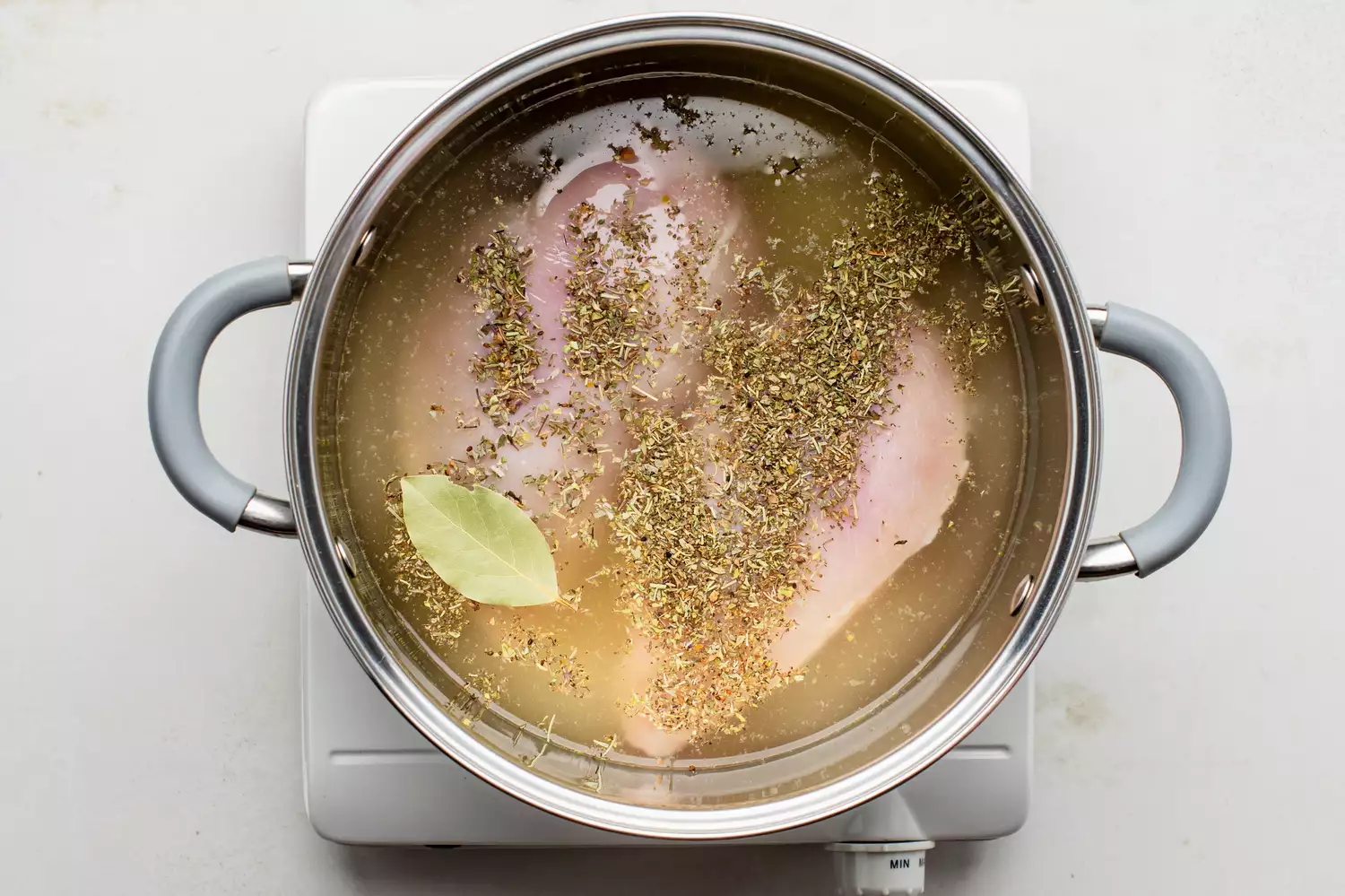 Poitrines de poulet avec des herbes en une seule couche dans une casserole, recouvertes de bouillon